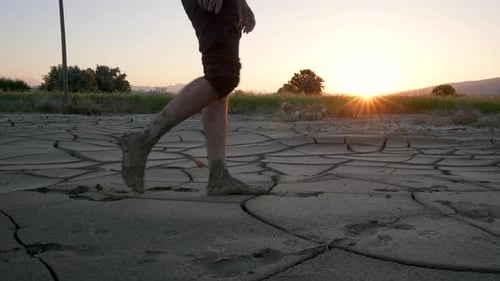 Man Walks Barefoot on Cracked Earth at Sunset