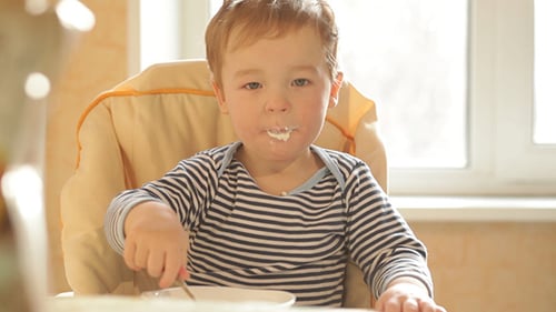 Boy Eating Food at Table in High Chair