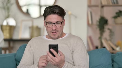 Man Sitting on Sofa Using Smartphone Celebrating