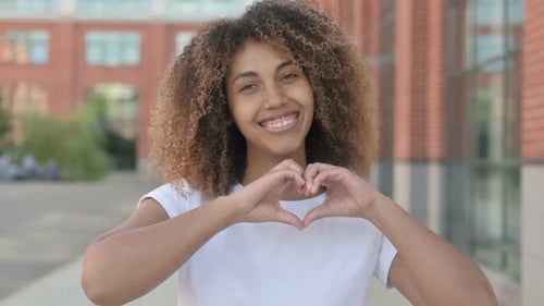 Woman Makes Heart Shape with Hands Outdoors