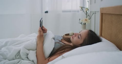 Girl Lies in Bed Looking at Smartphone