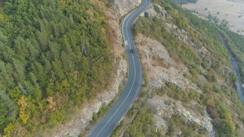 Drone Chasing Car Driving On Winding Road Through Green Forest On Mountain Slope