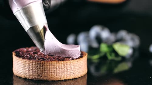 Pastry Chef Decorates Biscuit with Purple Cream From Pastry Bag, Close-up.