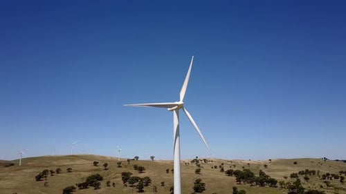 Pan around wind turbine to reveal windfarm on barren breezy hillside