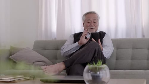 Ein Videoanruf asiatischer älterer Menschen mit Smartphone auf dem Sofa an einem entspannten Tag.