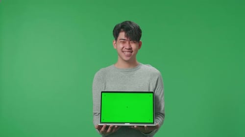 A Smiling Asian Man Saying Wow While Holding Green Screen Computer In The Green Screen Studio