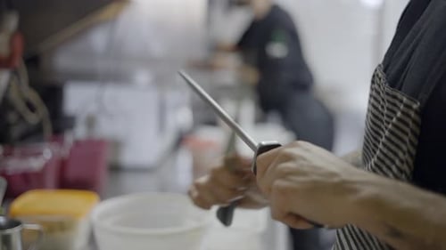Close Side View of Unrecognizable Chef Sharpening Knife in Kitchen