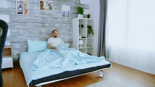 Man Working on Laptop in Bed at Home