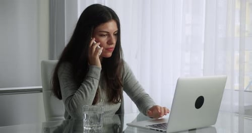 Woman Talking on Phone While Using Laptop