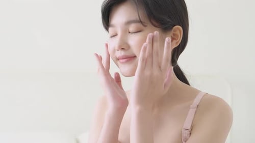 Woman Applying Lotion to Face in Bedroom