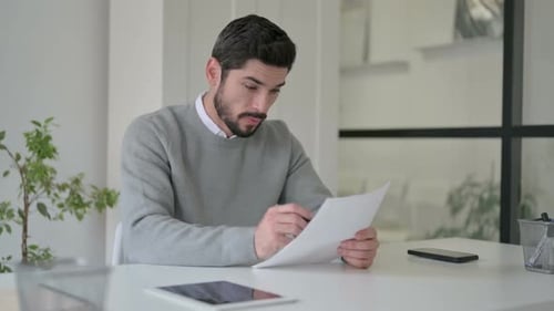 Young Man Celebrating Success While Reading Documents in Office