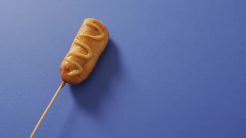 Video of corn dog with mustard on a blue surface