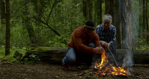 Handsome Guy Warms Hands at Campfire and Sits Near Father
