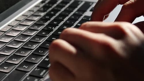 Hands typing on a laptop keyboard. High angle static close up shot