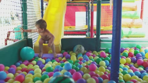 L'enfant joue dans la salle de jeux et descend le toboggan dans la piscine avec de petites balles