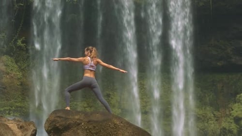 Slim Girl Poses on Round Rock Against Waterfall