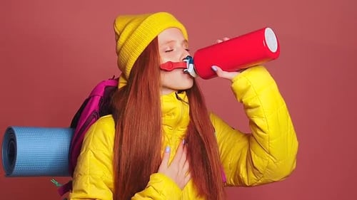 Tired Redhaired Ginger Woman in Pink Studio Background Wearing Yellow Windbreaker Jacket with Hat