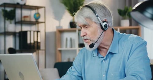 Senior Man Working Remotely on Laptop with Headset