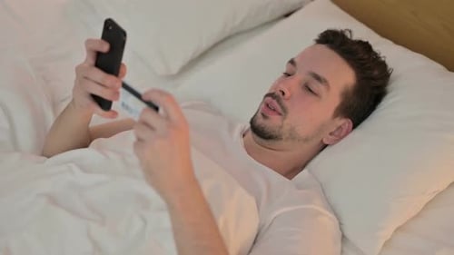 Young Man Shops Online in Bed with Phone