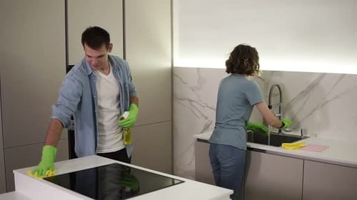 Young Married Couple in Casual Clothing and Both in Green Gloves Cleaning Kitchen After Moving to