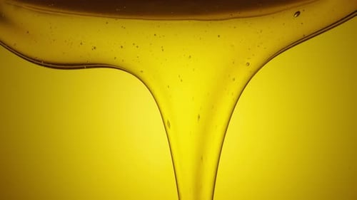 A Stream of Golden Thick Honey Spills on a Yellow Background