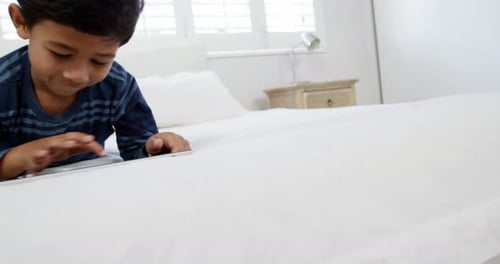 Boy using digital tablet while relaxing on bed