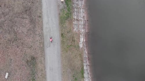 Cyclist riding near dam, drone top view. Woman in bike apparel cycling outdoor on gravel bike