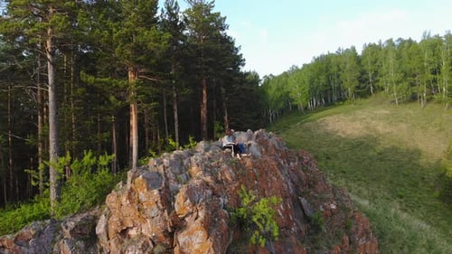 A Young Couple Sit on the Edge of a Cliff and Enjoy the Beautiful View