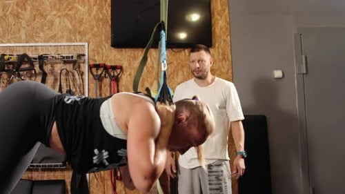 Woman Doing Suspension Exercise in Gym with Trainer
