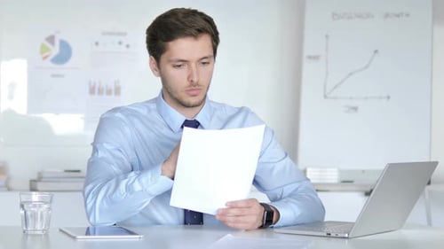 Young Adult Man Reviews Business Documents at Desk