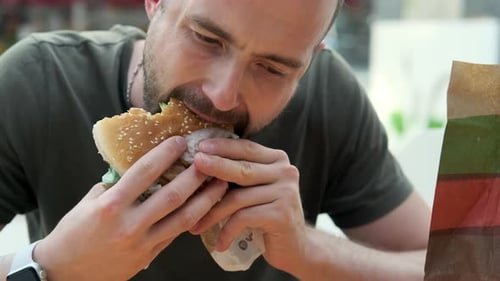 Bearded Man Enjoys Burger at an Urban Restaurant