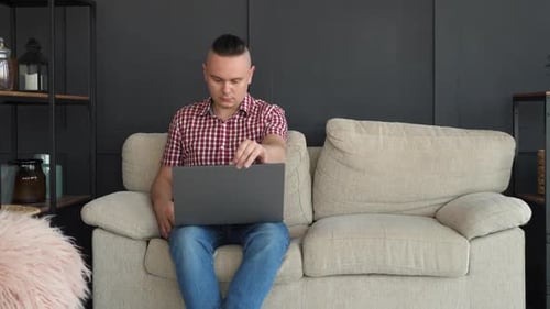 Man Opens Laptop and Works on Couch
