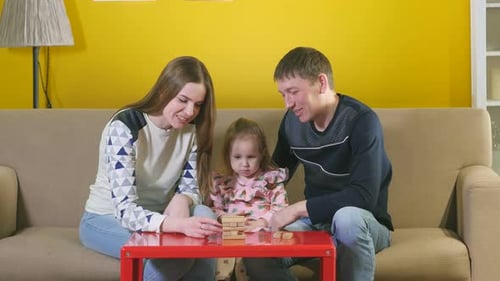 Mama und Papa spielen mit ihrer Tochter in einem Brettspiel auf der Couch. Hübscher Vater, schön