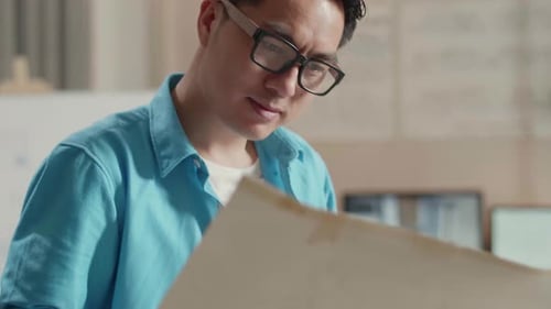 Close Up Of Asian Man Engineer With A Laptop Looking At Blueprint While Working At The Office