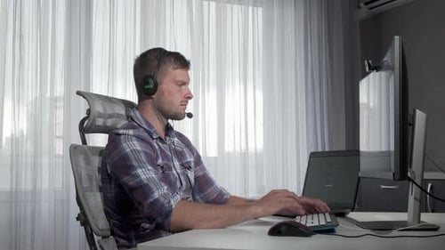 Man in Headset Working on Computer at Desk