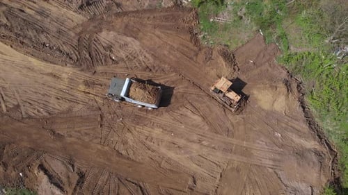 Top aerial view of bulldozer flattening surface on further construction site