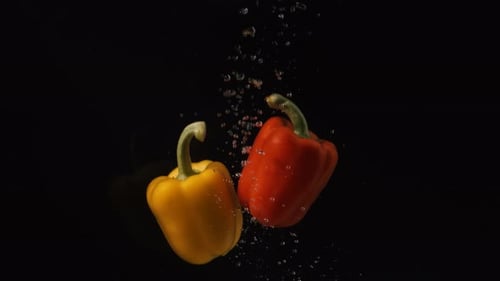 Red and Yellow Peppers Falling Into Water with Bubbles on Black Background. Vegetables Falling Into