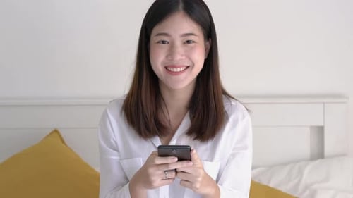 Smiling Woman Uses Smartphone in Bed
