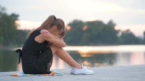 Sad Woman Sitting By the Lake at Sunrise
