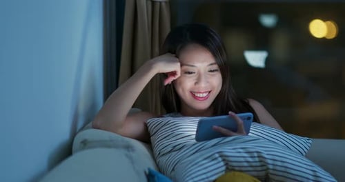 Smiling Woman Using Smartphone on Couch at Night