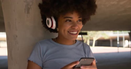 Mixed race woman listening music under bridge