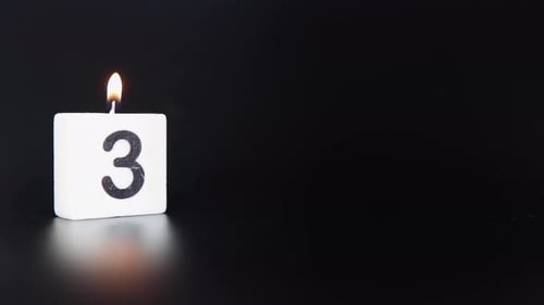 Una vela cuadrada que dice que el número 3 está encendido y apagado sobre un fondo negro oscuro