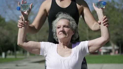 Senior Woman Exercising with Trainer in Park