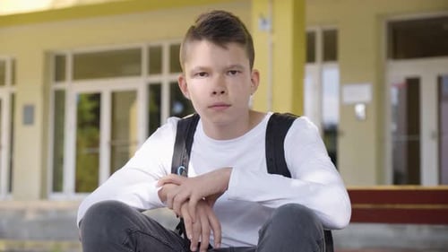 A Caucasian Teenage Boy Turns and Looks at the Camera As He Sits in Front of School Closeup