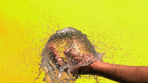Water Balloon Exploding in Hand on Yellow Background