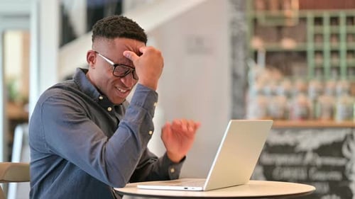 Stressed African Man with Laptop Having Headache in Cafe