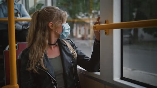 Woman Hipster in Protective Mask is Sitting in Moving Tram and Looking Out the Window