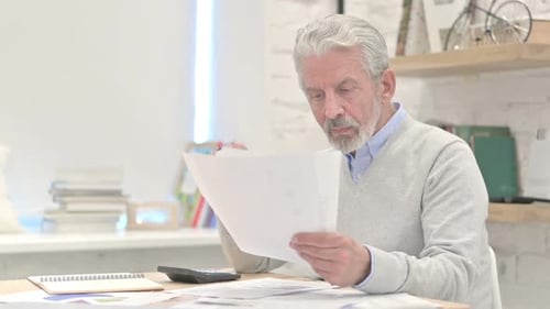 Man Reads Paperwork at Desk and Celebrates