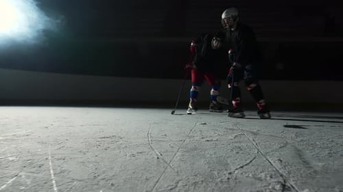 Two Sportsmen Hockey Players Who are Sliding on Ice Arena and Dribbles Hitting Puck with Stick