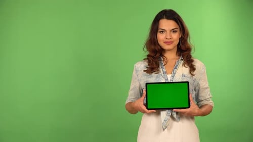 A Young Caucasian Woman Shows a Tablet with Green Screen to the Camera with a Smile Green Screen